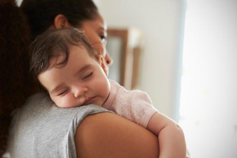 A person holds a sleeping baby against their shoulder